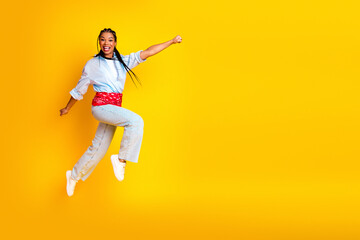 Obraz premium Young woman jumps with joy wearing denim and a red belt against a bright yellow backdrop