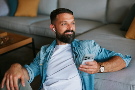 Man relaxing with smartphone and wireless earbuds listening to music