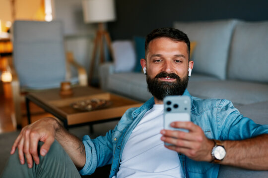 Man relaxing at home streaming content using smartphone earbuds
