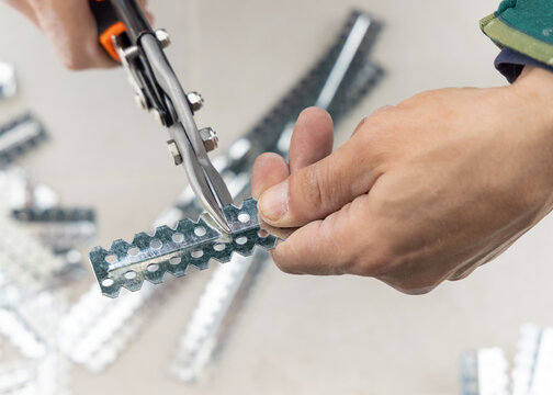 Drywall worker cutting metal profile with tin snips during suspended ceiling installation, hands close up