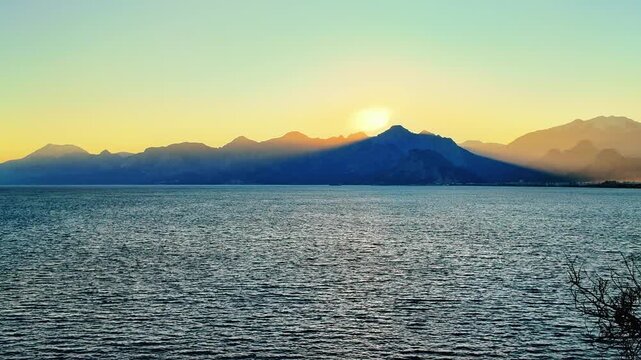Golden sunset behind taurus mountains silhouette over calm mediterranean sea in antalya turkey.