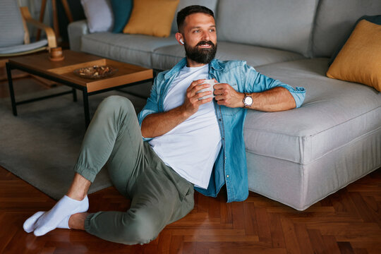 Relaxed man sitting on floor with coffee and wireless earbuds