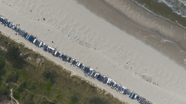 Aerial view of a long row of beach huts stretching across a wide sandy beach between grassy dunes and the North Sea in Velsen-Noord, North Holland, Netherlands.