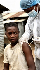 Fototapeta premium Woman doctor in protective suit administering vaccine to African teen boy in impoverished area. Medical help during virus pandemic. Vaccination campaign for children in rural setting.