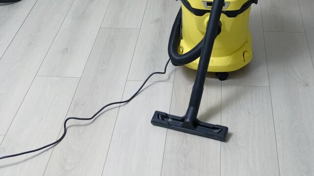 Efficient cleaning process using modern wired yellow vacuum cleaner with a black nozzle technology. No people. The white floor of the laminate is vacuumed. Vacuum cleaner cleaning wooden flooring.