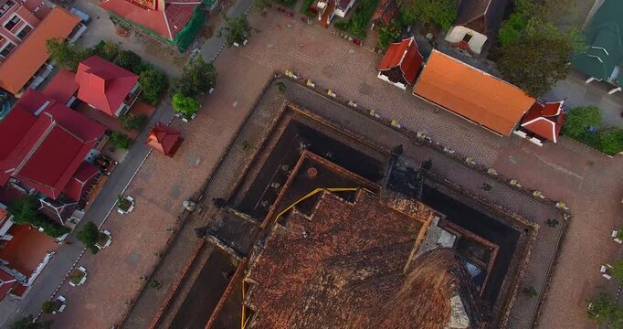 High angle drone shot capturing the grandeur of Wat Chedi Luang temple with its towering ancient stupa and beautifully crafted serpent statues along the stairway. Surrounded by old city walls