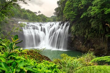Shifen Waterfall, often called the Little Niagara of Taiwan, in Pingxi District of New Taipei, Taiwan, cascades powerfully into a turquoise pool amid dense green foliage © Leonid Andronov