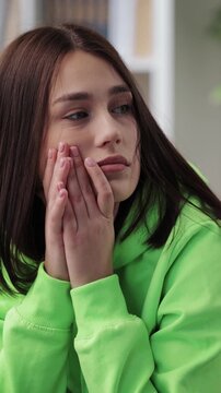 A woman sits deep in thought at home wearing a green hoodie while looking away.