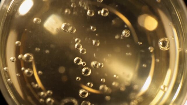Carbonated water bubbles rising in a glass. Close-up macro footage of sparkling water with golden bubbles. High-speed camera captures effervescence and fizz in slow motion.