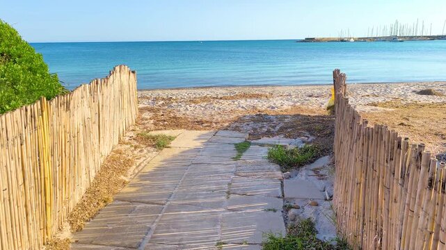 First person POV walk from a sandy path leading to the sea. Immersive coastal transition with beach scenery, blue water and summer travel atmosphere.