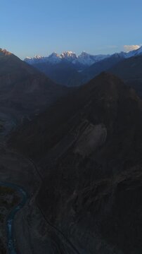 Aerial view of Hunza Valley featuring a winding river and rugged mountains with snow-capped peaks in the distance in Hunza Nagar, Gilgit Baltistan, Pakistan.