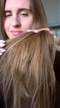 Close up of concerned woman inspecting dry brittle strands and split ends. Female assessing breakage, thinning and overall condition indoors. Beauty routine, scalp wellness, self care, recovery 