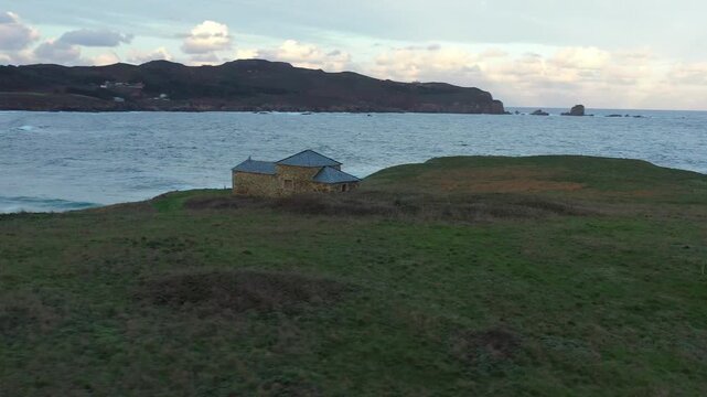 Aerial view of Ermita de Santa Comba on a grassy headland surrounded by the sea under a cloudy sky in Covas, La Coruna, Spain.