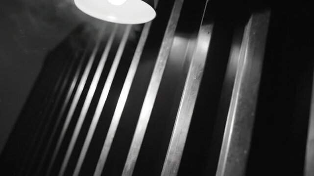 Dramatic monochromatic shot of a hanging lamp illuminating wooden slats with atmospheric fog and shadows