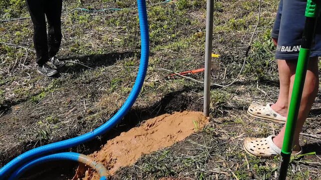 Two people drill a well to extract water and bring it to a house. Team members conduct soil testing at the construction site in clear weather. They use instruments to collect soil samples and analyze 