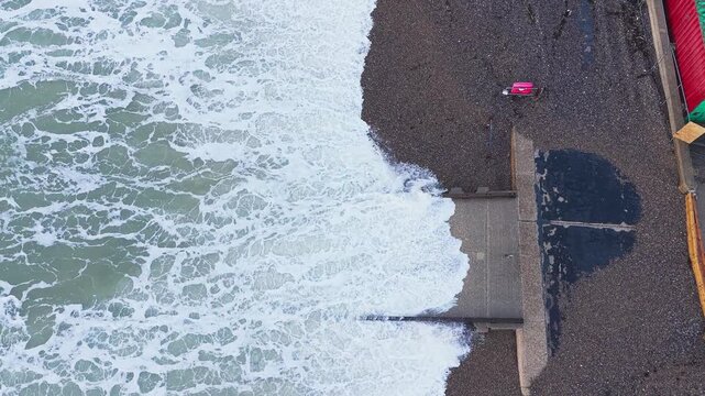 Waves surge over the boat ramp and stone-covered promenade at Freshwater Bay, Isle of Wight, during strong winds and rough sea conditions.