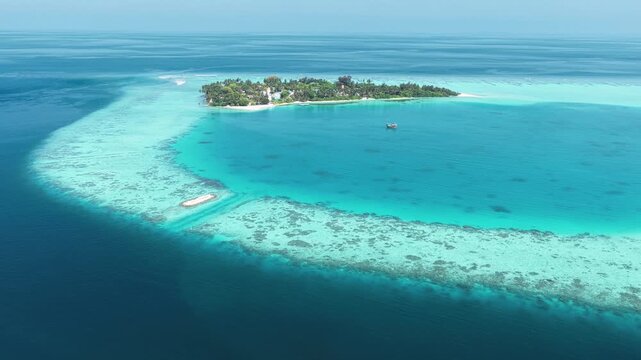Aerial view of a lush tropical island surrounded by a turquoise coral reef and crystal clear ocean waters in Kudahuvadhoo, Dhaalu Atoll, Maldives.