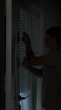 Mental health recovery and new beginning concept with young man opening blinds and window letting sunlight into dark apartment, emotional reset and fresh start, vertical video