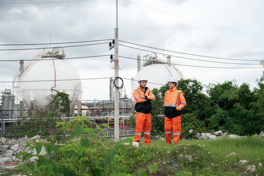 LNG storage tank inspection engineers using radio communication and mobile technology at industrial refinery site for safety compliance and operations control