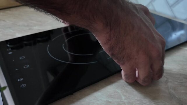 A hand removes a black induction hob from a countertop. The surface is light-colored and smooth, highlighting the sleek design of the hob.