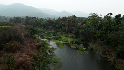 Obraz premium River flowing through wild green landscape with misty mountains in background