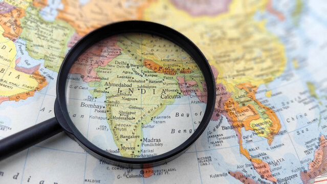 Magnifying glass focusing on India on a world map, representing travel, economic growth, geographic research, and international business opportunities.