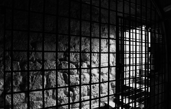 Black and white view of a medieval prison cell from inside the bars.