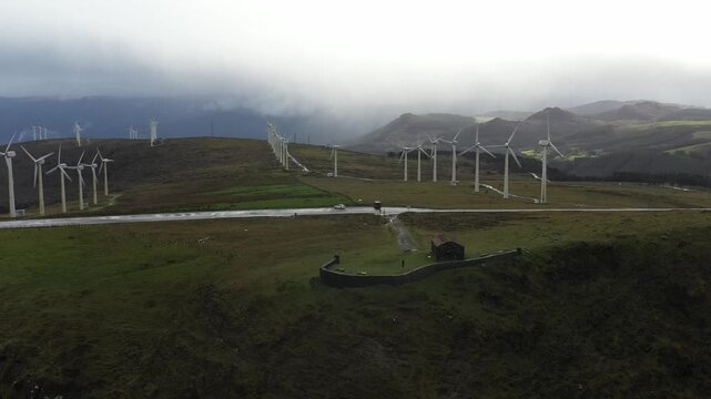 Aerial view of the Garita de Herbeira stone hut and wind turbines on a misty hillside under a cloudy sky in Meizoso, A Coruna, Spain.
