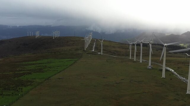 Aerial view of wind turbines standing on a grassy ridge under a cloudy sky near Garita de Herbeira in Meizoso, A Coruna, Spain.