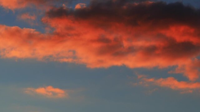 Timelapse A fiery red cloud in the blue sky. The wind moves the cloud at sunset