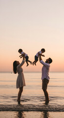 Fototapeta premium Happy Parents Lifting Children in Air during Golden Hour Beach Fun