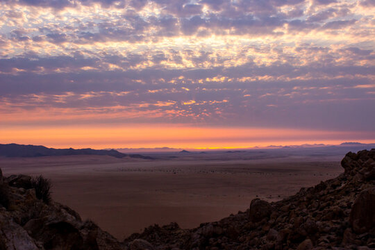 High altitude clouds, glowing silver in the light of the setting sun over the vas open barren plains of the Southern Namib desert in Namibia.