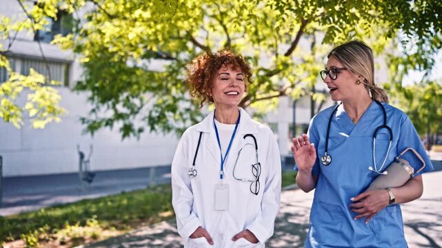 Two female doctors walking and talking outside a hospital