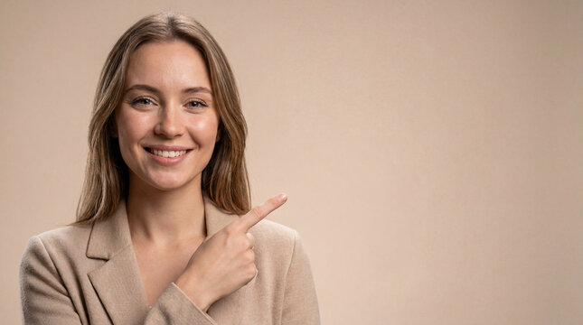 Woman in a beige blazer points towards the empty space to her side as she smiles at the camera.