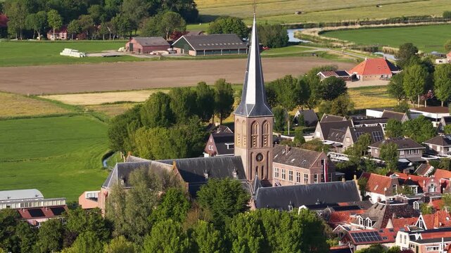 Aerial view of the historic St. Gertrude's Church surrounded by traditional red-roofed houses and lush green fields in Workum, Friesland, Netherlands.