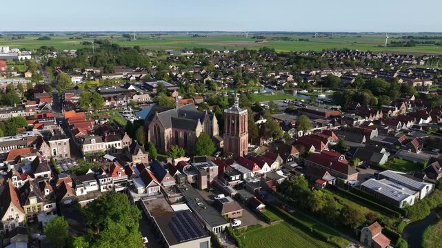 Aerial view of the historic Sint-Gertrudiskerk church and its brick bell tower surrounded by traditional red-tiled rooftops and lush green trees Workum, Friesland, Netherlands.