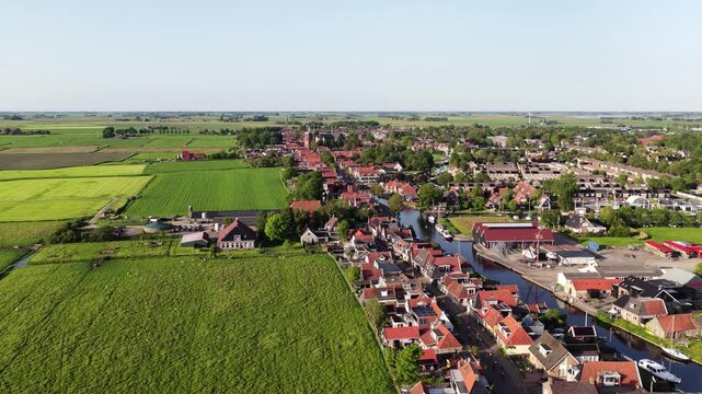 Aerial view of the historic town of Workum featuring traditional red-roofed houses, a narrow canal with boats, and lush green agricultural fields Workum, Friesland, Netherlands.