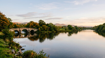 Obraz premium Stone arched bridge over a calm river during autumn sunset