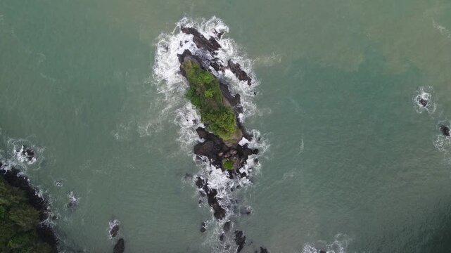 Aerial view of Pantai Karang Agung Kebumen with waves crashing against the rocky formation and lush greenery in Ayah, Central Java, Indonesia.