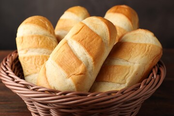 Naklejka premium Loaves of fresh bread in wicker basket on wooden table, closeup