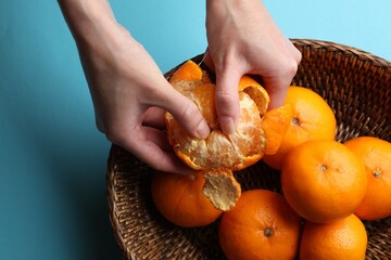 Woman peeling ripe tangerine and fresh fruits on light blue background, top view