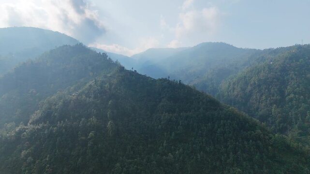 An atmospheric, high-contrast drone shot of a remote mountain hamlet settled deep inside a misty, shadowed alpine valley of the Eastern Himalayas.
