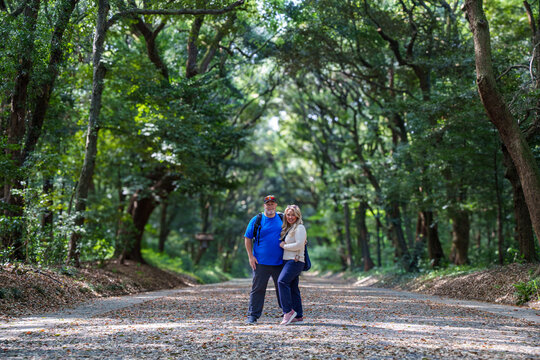 Couple poses in front along a tree lined walkway leading to Meiji Shinto shrine in Shibuya, Tokyo, Japan