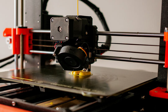 Close up of desktop 3D printer extruder head printing yellow plastic model on a steel heated bed