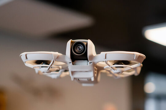 Macro shot of standalone lightweight camera drone flying inside a modern office room with blurred ceiling lights