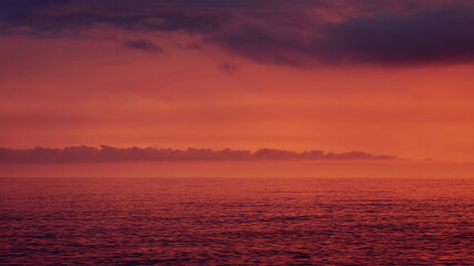 Obraz premium A breathtaking minimalist seascape at sunset in Scalea, Italy. The dramatic red and purple sky is filled with dark clouds, beautifully reflecting over the calm waters of the Mediterranean Sea.