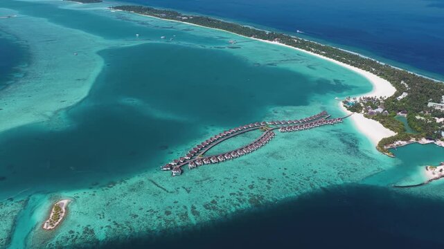 Aerial view of luxury overwater bungalows arranged in curved pattern over a turquoise lagoon with white sand beaches and tropical greenery in Kudahuvadhoo, Dhaalu Atoll, Maldives.