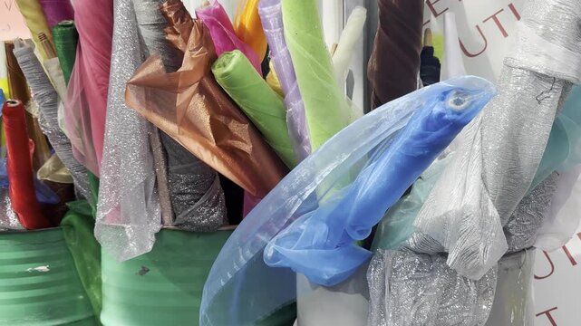 View of colorful fabrics and sheer tulle of different textures displayed in rolls inside a fabric store. A wide assortment of textiles highlights variety in materials, colors, and patterns used for ta