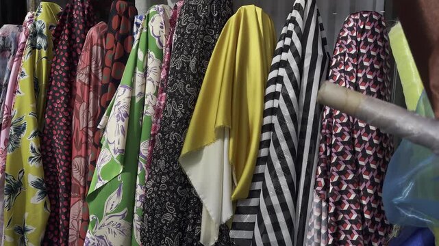 View of colorful yellow and red fabrics and sheer tulle of different textures displayed in rolls inside a fabric store. The assortment highlights a variety of materials and shades used for sewing, tai