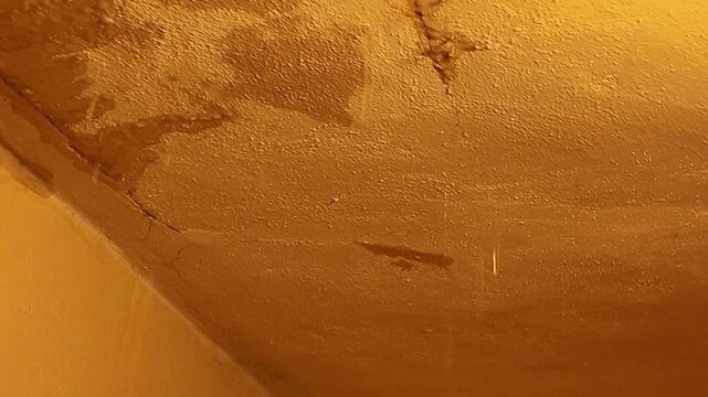 Close-up of textured wall with water stains and cracks, showing signs of damage. Detailed view of a textured wall surface exhibiting water damage, cracks, and discoloration, suggesting structural
